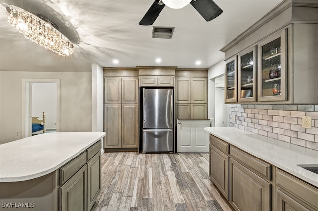 kitchen featuring a center island, backsplash, stainless steel fridge, ceiling fan with notable chandelier, and hardwood / wood-style flooring