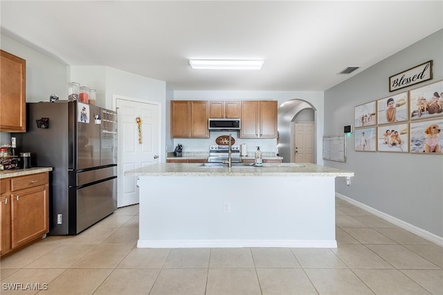 kitchen featuring light stone countertops, a kitchen island with sink, light tile patterned flooring, and stainless steel appliances