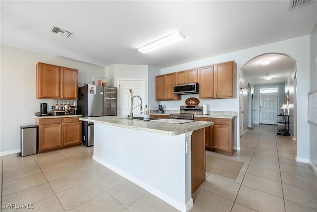 kitchen with sink, light tile patterned floors, stainless steel appliances, and a center island with sink