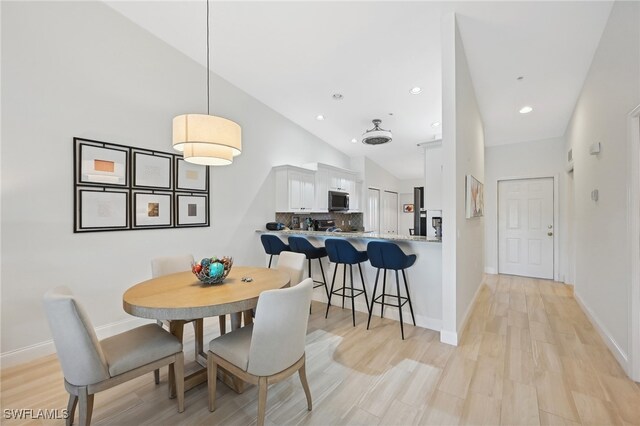 dining area featuring high vaulted ceiling and light hardwood / wood-style flooring