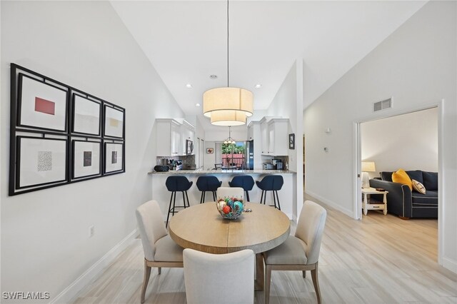 dining area featuring high vaulted ceiling and light hardwood / wood-style floors