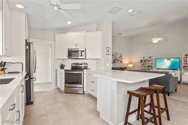 kitchen featuring kitchen peninsula, lofted ceiling, a breakfast bar, white cabinets, and appliances with stainless steel finishes