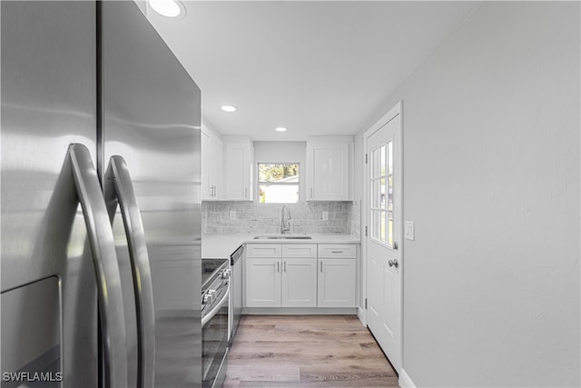 kitchen featuring backsplash, stainless steel appliances, sink, light hardwood / wood-style floors, and white cabinetry