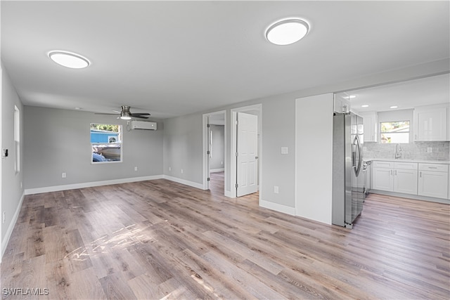 unfurnished living room with a wealth of natural light, ceiling fan, light hardwood / wood-style floors, and a wall mounted air conditioner