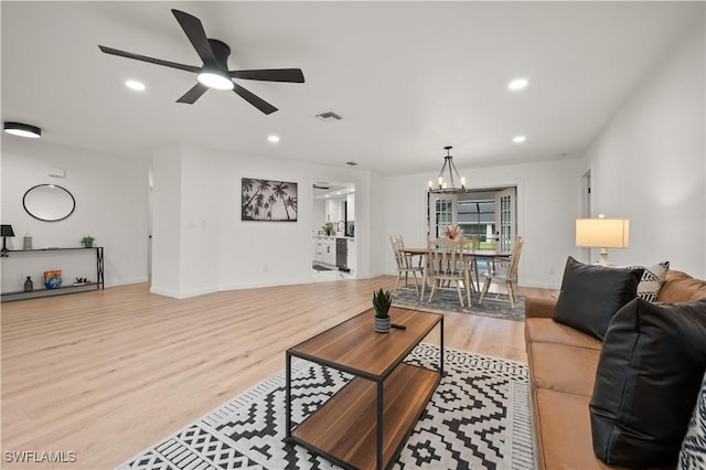 living room with ceiling fan with notable chandelier and light hardwood / wood-style flooring