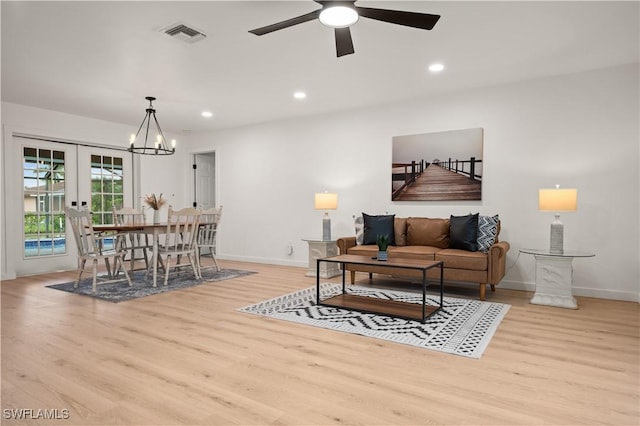 living room featuring french doors, ceiling fan with notable chandelier, and light hardwood / wood-style floors