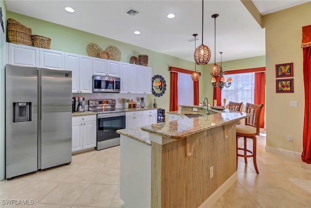 kitchen featuring a kitchen bar, appliances with stainless steel finishes, a center island with sink, decorative light fixtures, and white cabinets