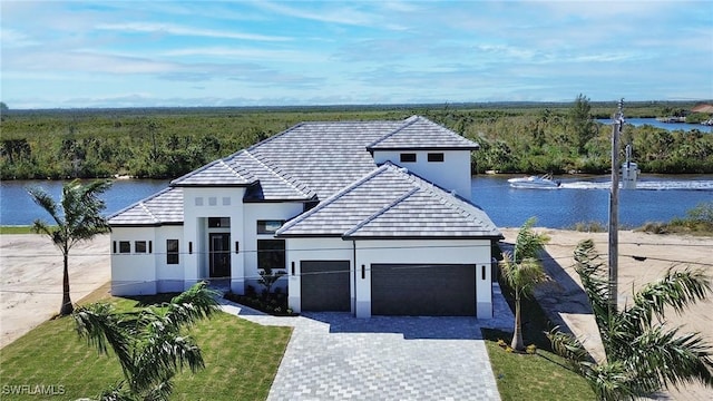 view of front facade featuring a garage, decorative driveway, a water view, and stucco siding