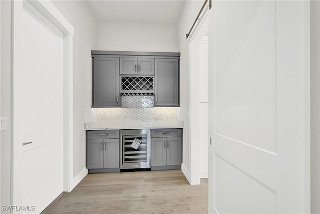 bar featuring a dry bar, beverage cooler, a barn door, decorative backsplash, and light wood-style floors