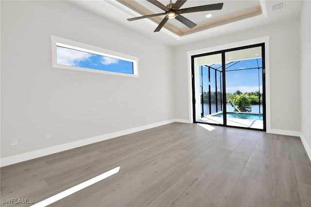 empty room with a tray ceiling, visible vents, a ceiling fan, wood finished floors, and baseboards