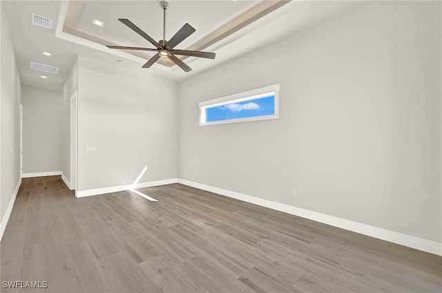 empty room with a raised ceiling, visible vents, baseboards, and wood finished floors