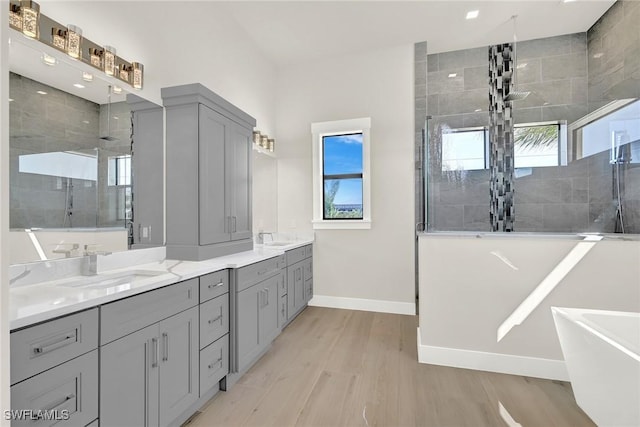 full bath featuring double vanity, a walk in shower, a sink, and wood finished floors