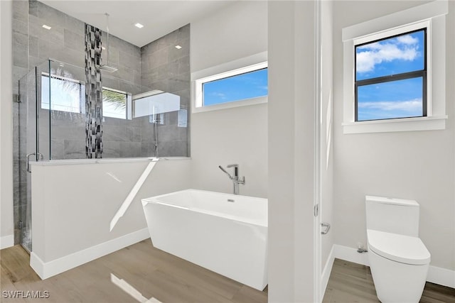 bathroom with baseboards, toilet, a soaking tub, wood finished floors, and a shower stall