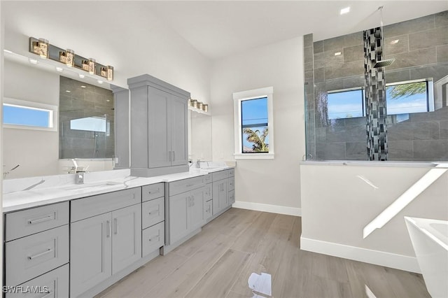 full bathroom with a walk in shower, double vanity, a sink, and baseboards