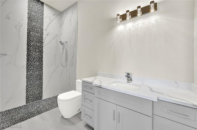 bathroom with tiled shower, vanity, and toilet