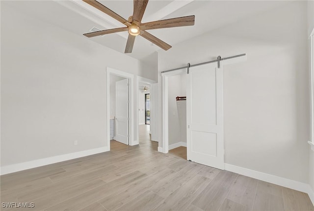 unfurnished bedroom featuring light wood-style floors, a barn door, baseboards, and a ceiling fan