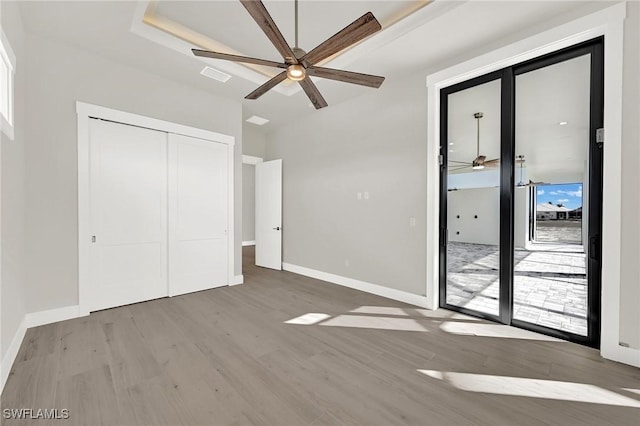 unfurnished bedroom featuring ceiling fan, access to exterior, wood-type flooring, and a closet