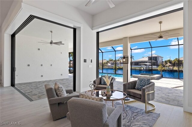 living room with ceiling fan, a water view, and light hardwood / wood-style floors