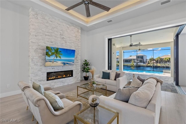 living room with ceiling fan, a stone fireplace, and light wood-type flooring