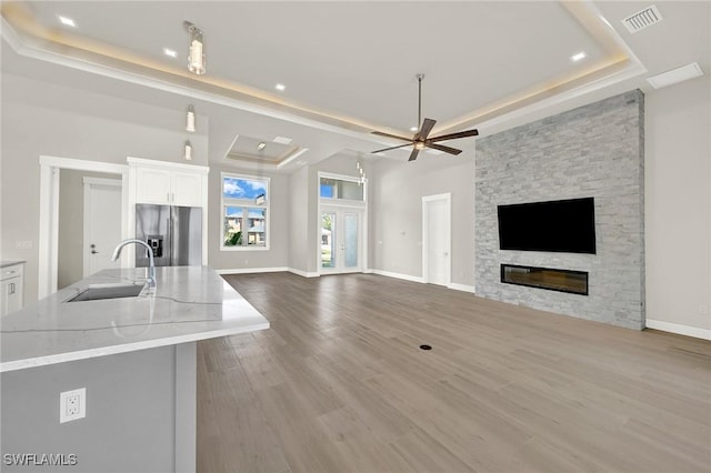 unfurnished living room featuring a fireplace, a raised ceiling, visible vents, a sink, and wood finished floors