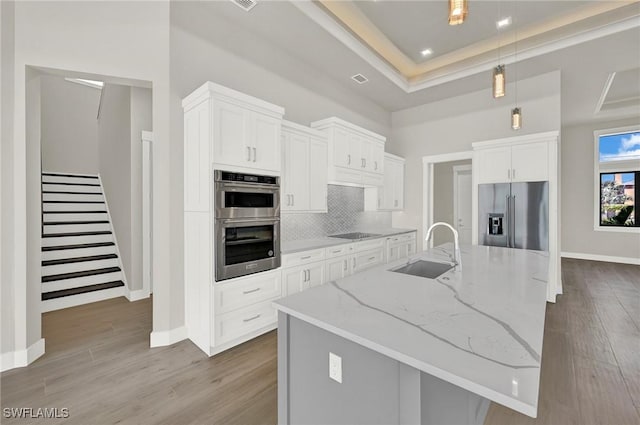 kitchen with stainless steel appliances, wood finished floors, a sink, and tasteful backsplash