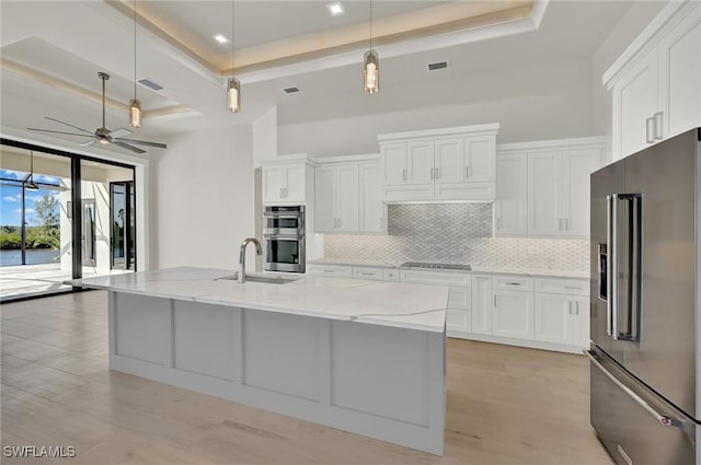 kitchen featuring a raised ceiling, white cabinets, stainless steel appliances, and decorative light fixtures