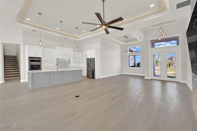 unfurnished living room featuring a towering ceiling, baseboards, visible vents, light wood-style floors, and a raised ceiling