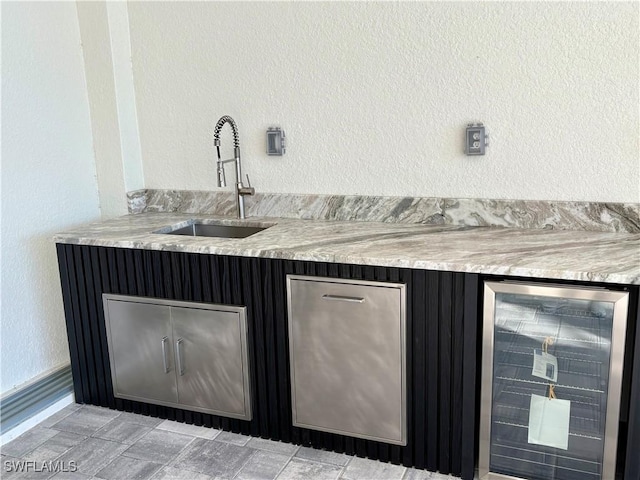 bar featuring beverage cooler, a textured wall, and a sink