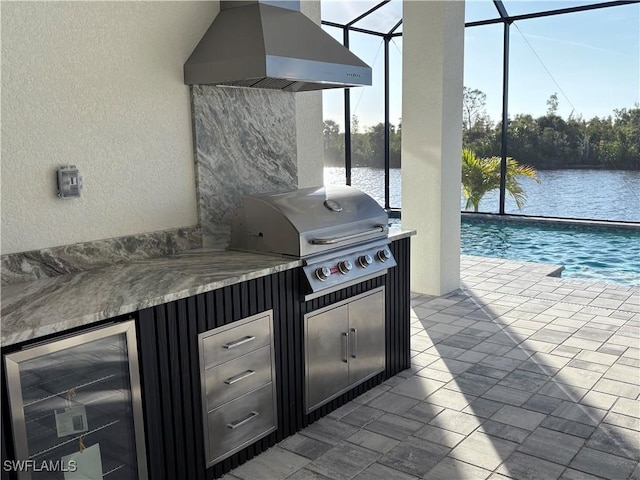 view of patio featuring glass enclosure, a water view, an outdoor bar, area for grilling, and beverage cooler