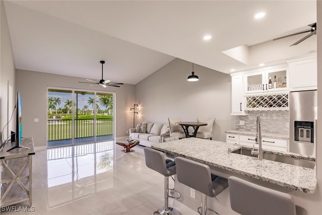 kitchen with stainless steel refrigerator with ice dispenser, light stone counters, a breakfast bar, white cabinetry, and hanging light fixtures