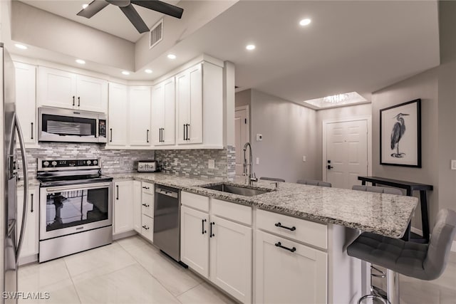 kitchen featuring a breakfast bar, white cabinets, sink, light stone counters, and stainless steel appliances