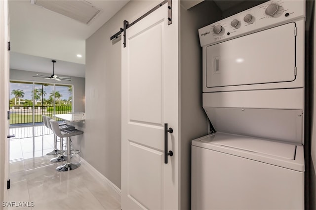 washroom with a barn door, stacked washer and dryer, ceiling fan, and light tile patterned flooring