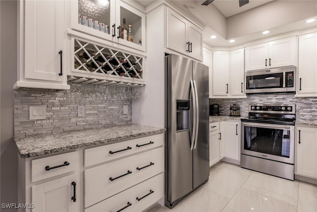 kitchen featuring light stone countertops, decorative backsplash, white cabinetry, and stainless steel appliances