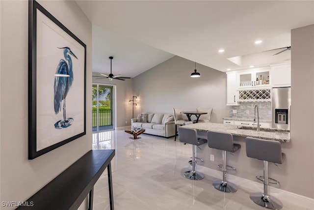 kitchen with stainless steel refrigerator with ice dispenser, a kitchen breakfast bar, light stone counters, sink, and white cabinetry