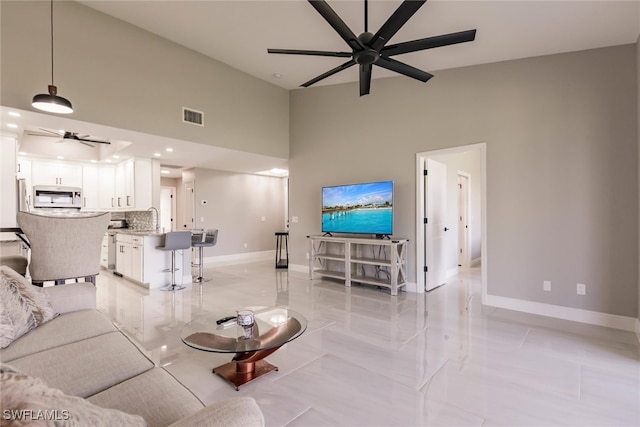 living room featuring ceiling fan, sink, light tile patterned floors, and a high ceiling