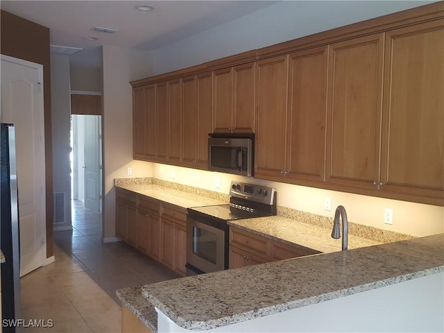 kitchen featuring light stone counters, light tile patterned floors, kitchen peninsula, and appliances with stainless steel finishes