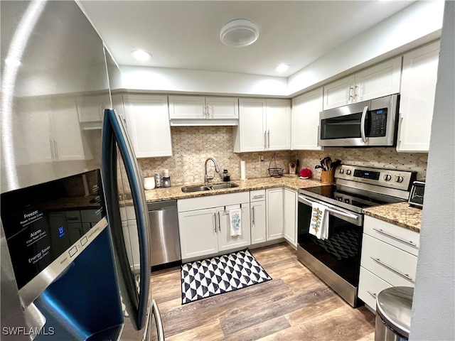 kitchen featuring decorative backsplash, appliances with stainless steel finishes, sink, light hardwood / wood-style floors, and white cabinetry