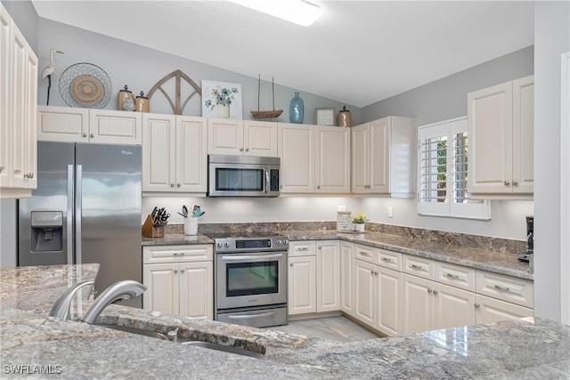 kitchen with light stone countertops, sink, lofted ceiling, and appliances with stainless steel finishes