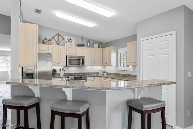 kitchen featuring kitchen peninsula, appliances with stainless steel finishes, a breakfast bar, and vaulted ceiling