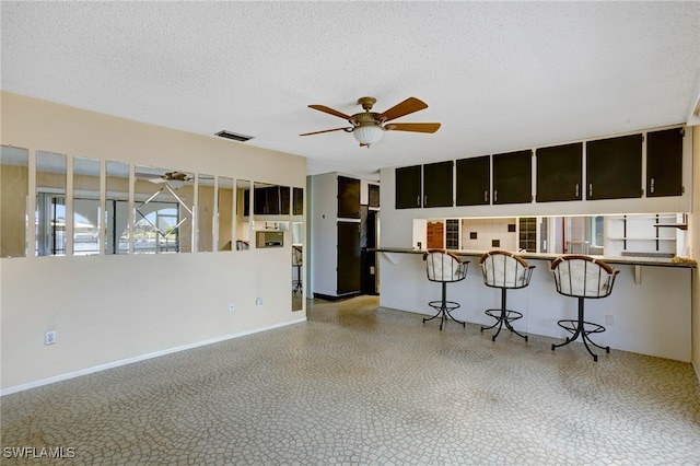 interior space with kitchen peninsula, ceiling fan, a breakfast bar, and a textured ceiling