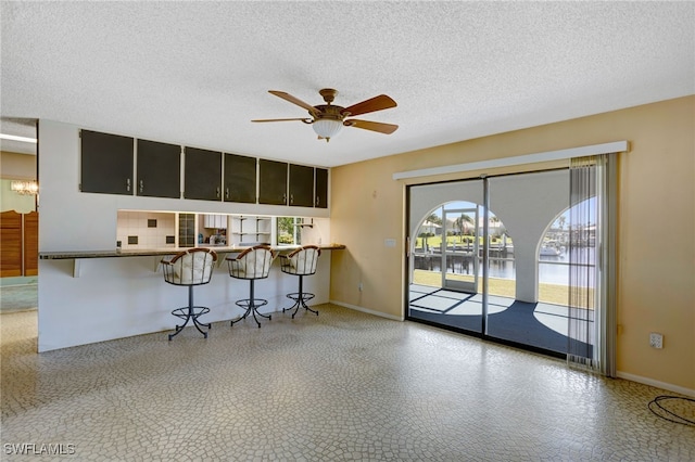 kitchen featuring a kitchen bar, ceiling fan, a water view, and a textured ceiling