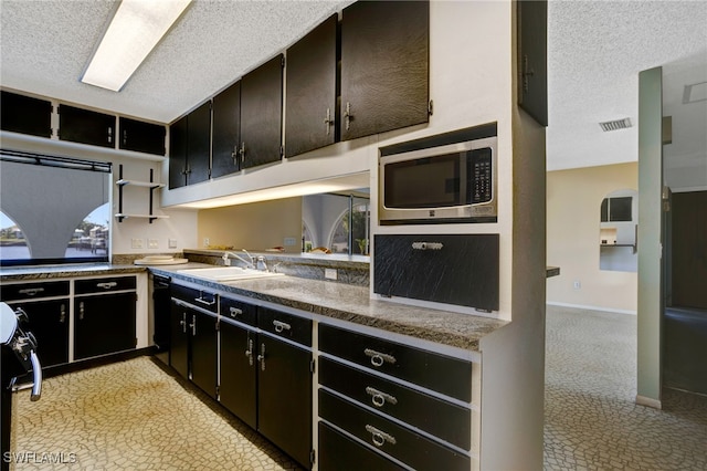 kitchen with a textured ceiling, stainless steel microwave, and sink