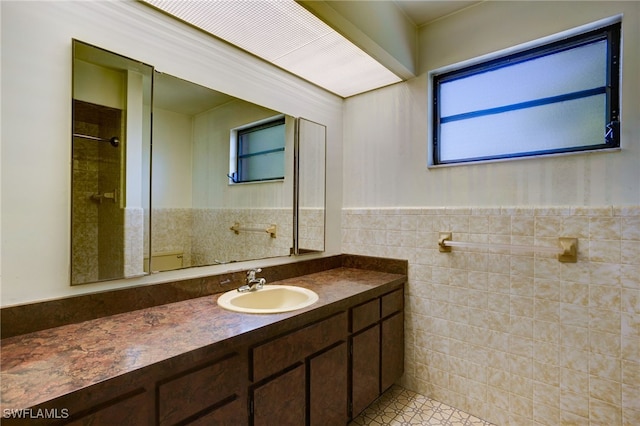 bathroom with tile patterned floors, a tile shower, vanity, and tile walls