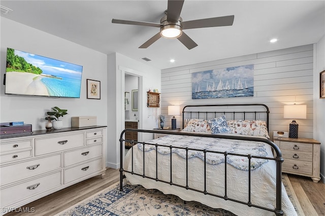 bedroom featuring ceiling fan, light wood-type flooring, and wooden walls