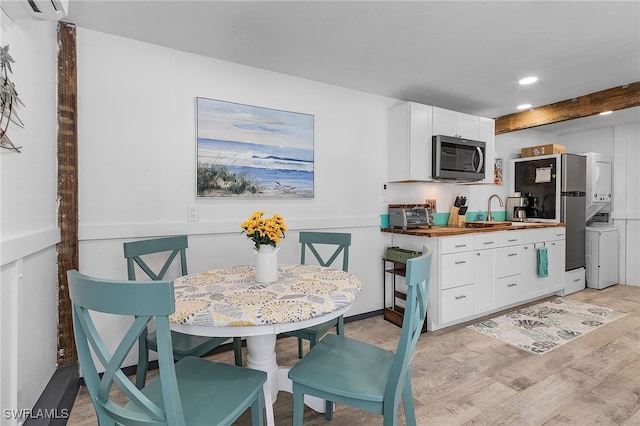 kitchen with white cabinetry, stainless steel appliances, wooden counters, light hardwood / wood-style floors, and stacked washer / drying machine