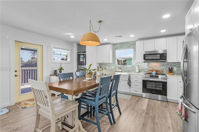 kitchen featuring appliances with stainless steel finishes, light wood-type flooring, stacked washing maching and dryer, decorative light fixtures, and white cabinetry