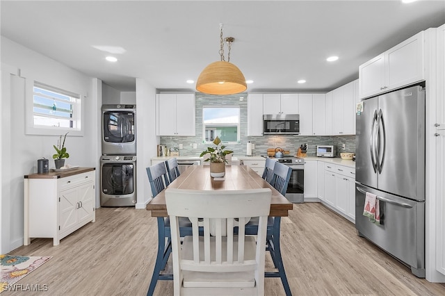 kitchen with light hardwood / wood-style floors, stainless steel appliances, decorative light fixtures, white cabinets, and stacked washer and dryer