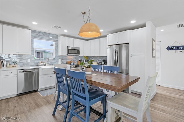 kitchen with appliances with stainless steel finishes, light wood-type flooring, white cabinetry, and hanging light fixtures