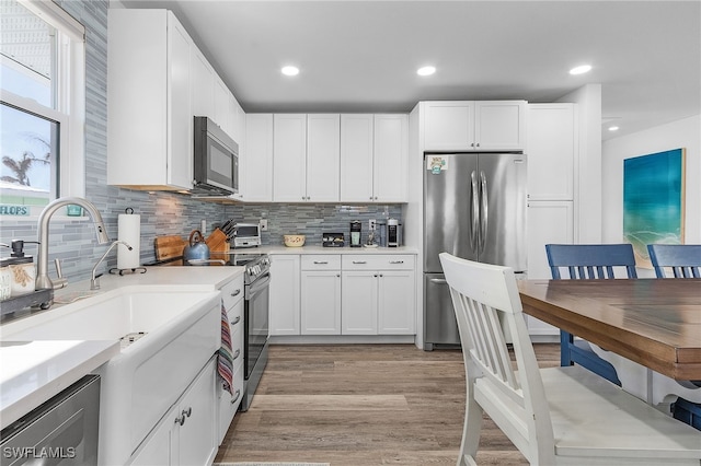 kitchen with white cabinets, decorative backsplash, light wood-type flooring, and stainless steel appliances