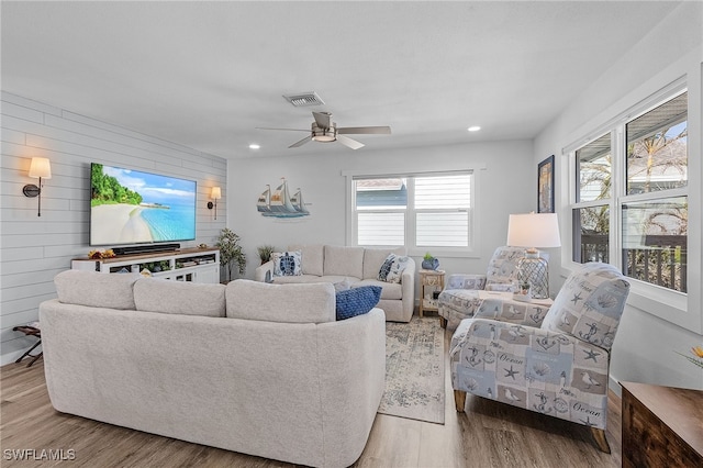 living room with ceiling fan, wooden walls, and light hardwood / wood-style floors